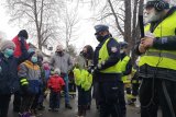 Policjantka i redaktor radiowy rozmawiają z dziećmi. Jedno z dzieci podnosi rękę do góry, aby zabrać głos.
