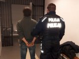 Umundurowany policjant trzyma podejrzanego przed celą.