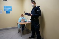 Umundurowany policjant stoi przy punkcie rejestracji szczpień, przy stoliku siedzi pielęgniarka.