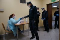 Umundurowany policjant podaje pielęgniarce w punkcie szczepień wypełnioną ankietę.