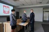 Policjant w mundurze wyjściowym składa gratulację policjantowi i podaję mu rękę. Na pierwszym planie stoi policjanta w mundurze wyjściowym.