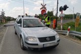 Policjanci i pracownicy kolei rozmawiają z kierowcą samochodu osobowego w rejonie przejazdu kolejowego.