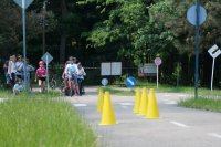 Na pierwszym planie pachołki imitujące przeszkodę drogową. W tle stoją dzieci na rowerach. Zdjęcie zrobione na ścieżce edukacyjnej w miasteczku rowerowym.