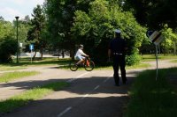 Policjant z ruchu drogowego obserwuję ucznia jadącego rowerem podczas egzaminu na kartę rowerową. Zdjęcie zrobione na ścieżce edukacyjnej w miasteczku rowerowym.