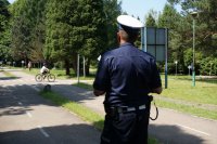 Policjant z ruchu drogowego obserwuję ucznia jadącego rowerem podczas egzaminu na kartę rowerową. Zdjęcie zrobione na ścieżce edukacyjnej w miasteczku rowerowym.