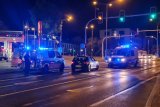 Na skrzyżowaniu stoją dwa policyjne radiowozy na sygnałach. W jednym z nich z tyły w przedziale dla osób zatrzymanych siedzi osoba. 
Zdjęcie wykonane w nocy.