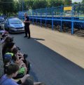 Policjant dzielnicowy rozmawia z dziećmi siedzącymi na trybunie stadionu piłkarskiego.