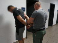 Policjant nieumundurowany zakłada zatrzymanemu kajdanki na ręce z tyłu.