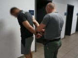 Policjant nieumundurowany zakłada zatrzymanemu kajdanki na ręce z tyłu.