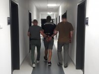 Policjanci nieumundurowani prowadzą zatrzymanego mężczyznę przez korytarz na komendzie.