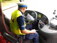 Policjant z ruchu drogowego siedząc za kierownicą autokaru sprawdza stan techniczny pojazdu