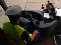 Policjant z ruchu drogowego siedząc za kierownicą autokaru sprawdza stan techniczny pojazdu