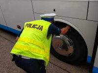 Policjant z ruchu drogowego sprawdza dłonią bieżnik opony autokaru