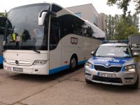 Na parkingu stoi autokar, a obok niego policyjny radiowóz ruchu drogowego.