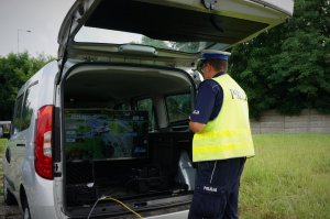 Umundurowany policjant ruchu drogowego obserwuje ekran monitora umieszczonego w części bagażowej busa.