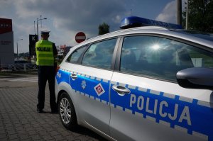 Widok na policyjny radiowóz, w tle stoją policjanci.