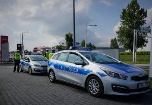 Policyjne radiowozy stoją na parkingu przy drodze, w tle policjanci z ruchu drogowego.