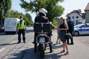 Policjanci z drogówki prowadzą akcję profilaktyczną na drodze, z uczestnikami ruchu drogowego.