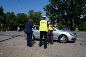 Policjanci z drogówki prowadzą akcję profilaktyczną na drodze, z uczestnikami ruchu drogowego.