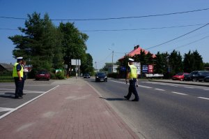 Policjanci z drogówki prowadzą akcję profilaktyczną na drodze, z uczestnikami ruchu drogowego.