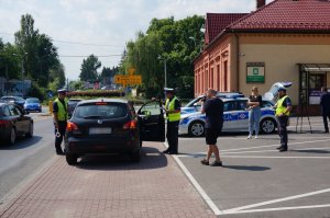 Policjanci z drogówki prowadzą akcję profilaktyczną na drodze, z uczestnikami ruchu drogowego.