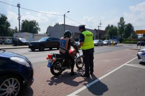 Policjanci z drogówki prowadzą akcję profilaktyczną na drodze, z uczestnikami ruchu drogowego.