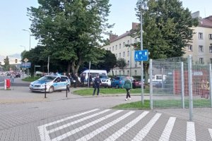 Policjanci stoją w okolicy stadionu miejskiego podczas zabezpieczenia meczu piłkarskiego. Zdjęcie wykonane w pogodny dzień.