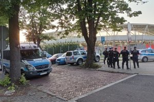 Policjanci stoją w okolicy stadionu miejskiego podczas zabezpieczenia meczu piłkarskiego. Zdjęcie wykonane w pogodny dzień.