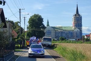 Policyjny radiowóz jedzie przed pieszą pielgrzymką, w tle wieża kościoła