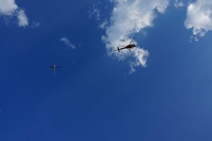 Widok na niebo od dołu, na tle błękitnego nieba dwa helikoptery i dron.