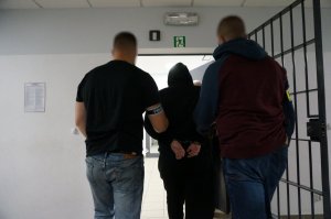 Nieumundurowani policjanci wyprowadzają zatrzymanego mężczyznę z pomieszczenia.