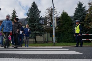 Policjant stoi obok przejścia dla pieszych, którym przechodzą dzieci.