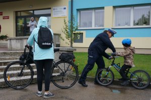 Policjantka ruchu drogowego rozmawia z dzieckiem na rowerze, stoją przed szkołą podstawową.