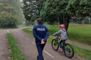 Policjant ruchu drogowego obserwuje ucznia jadącego na rowerze podczas egzaminu.