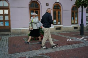 Uśmiechnięta kobieta idąca z odblaskiem założonym na rękawie. W przeciwnym kierunku przechodzi mężczyzna