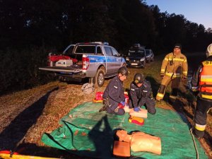 Policjanci i strażacy trenują udzielanie pierwszej pomocy na fantomach. Zdjęcie wykonane w nocy, w lesie.