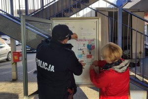 Policjant razem z członkiem rady osiedla wieszają plakat na tablicy informacyjnej.