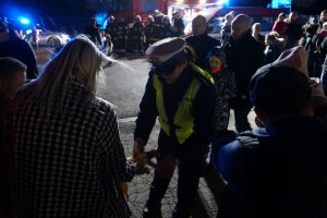 Policjantka z ruchu drogowego zakłada dziecku opaskę odblaskową na rękaw. Obok inni uczestnicy akcji. Zdjęcie wykonane w nocy.