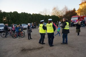 Policjantki rozdają odblaski podczas akcji profilaktycznej. Na drugim planie strażacy ochotnicy.