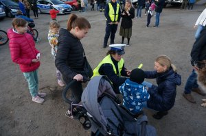 Policjantki rozdają odblaski podczas akcji profilaktycznej. Na drugim planie strażacy ochotnicy.