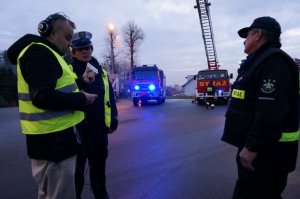 Policjantka z ruchu drogowego udziela wywiadu radiowego. Obok strażak ochotnik. Zdjęcie wykonane na płycie parkingu.