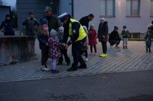 Policjantka z ruchu drogowego rozdaje uczestnikom akcji profilaktycznej opaski odblaskowe.