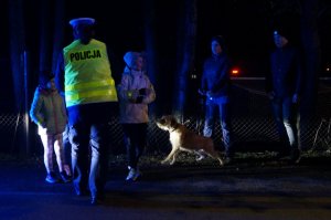 Policjantka rozdaje opaski odblaskowe dzieciom podczas akcji profilaktycznej. Zdjęcie wykonane po zmroku.