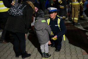 Policjantka kuca przy dziecku i daje mu opaskę odblaskową.
