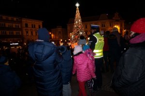 Policjantka stoi razem z dziećmi. W tle choinka miejska.