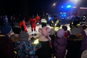 Policjantki z drogówki rozmawiają z grupką dzieci na parkingu. Zdjęcie wykonane po zmroku.