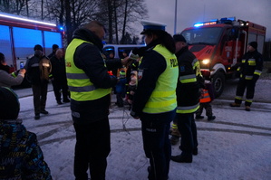 Policjantka ruchu drogowego udziela wywiad radiowego. W tle wozy strażackie i radiowóz policyjny. Zdjęcie wykonane w dzień na parkingu.