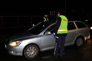 Policjanci kontrolują stan trzeźwości kierowcy alkomatem. Zdjęcie wykonane na drodze, o zmierzchu.