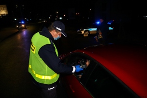 Policjanci kontrolują stan trzeźwości kierowcy alkomatem. Zdjęcie wykonane na drodze, o zmierzchu.