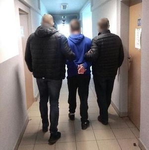 Nieumundurowani policjanci prowadzą zatrzymanego korytarzem komisariatu.